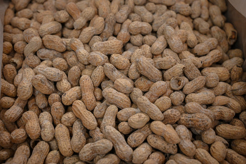 A close-up view of many whole peanuts in their natural tan-brown shells, filling the frame.