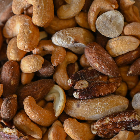 A close-up pile of mixed nuts including cashews, almonds, pecans, and peanuts with a light dusting of salt
